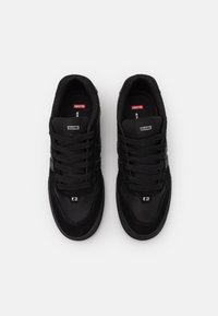 Chaussures de sport noires avec une tige en combinaison de suède et de mesh, lacets plats et marquage de la marque sur la languette et sur le côté. Semelle texturée.