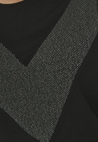 Černý top s V-š shape designem a stříbrnými metalickými ozdobami vytvářejícími texturovaný vzor. Hladká látka s těsným střihem.