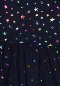 Námořnické šaty z látky s multibarevnými hvězdnými flitry, se skládáním na volánkovém lemu. Iridescentní hvězdy různých velikostí rozmístěné po celém šatech.
