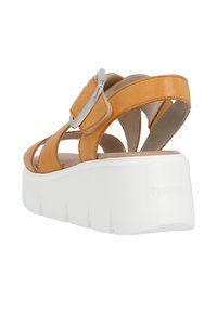 Sandale en cuir tan avec semelle plateforme blanche. Équipée d'une boucle réglable et d'un design ouvert avec plusieurs bretelles. Semelle intérieure texturée visible.