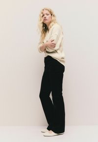 Creme strikket sweater, sort kordfløjs flared bukser og lyse sko. Teksturen af sweateren er blød og luftig.