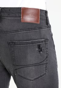 Mörkgrå denimjeans med en slitna ficka, läderbakpatch med varumärkeslogotyp och standarddesign med fem fickor.