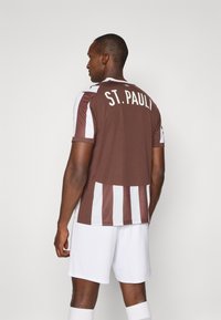 Brun og hvid stribet fodboldtrøje med 'ST. PAULI' i hvid på ryggen. Letvægtsstof med korte ærmer og rund halsdesign.