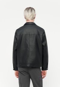 Black leather jacket with a collar, snap buttons, and a textured finish. Features a relaxed shape, reaching mid-hip and long sleeves.