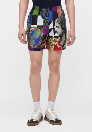 Personne portant un short à motifs multicolores avec un buste classique et des motifs décoratifs, des chaussettes blanches et des baskets blanches et noires.