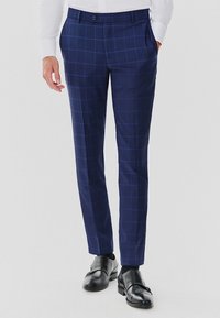 Granatowe spodnie w kratkę o dopasowanym kroju, z płaskim przodem, bocznymi kieszeniami i gładką fakturą. Noszone z czarnymi butami.