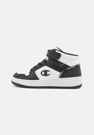 Baskets montantes noir et blanc avec lacets, bride velcro, logo Champion sur le côté et le talon, semelle texturée sur fond blanc.