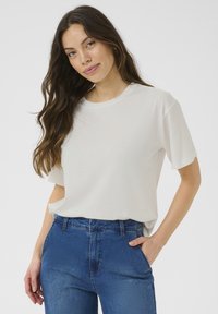 Hvid T-shirt med korte ærmer i blød stof, der har en rund halsudskæring og en afslappet pasform, parret med blå denimjeans.