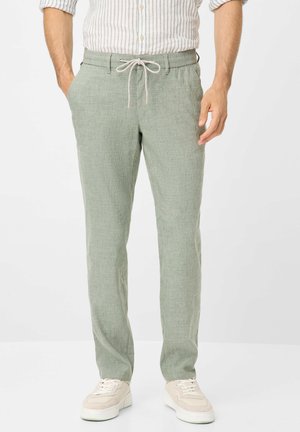 Lichtgroene linnen broek met een ontspannen pasvorm, elastische tailleband en trekkoord. Draagt met beige sneakers en een gestreepte overhemden.