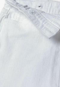 Vita denimjeans med knäppning, en liten framficka och bälteshällor. Tyget har en slät yta med subtila sömdetaljer.