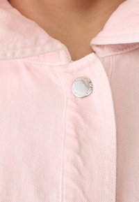 Chaqueta de denim rosa con cuello, que presenta cierres a presión plateados y detalles de costura visibles en el tejido.