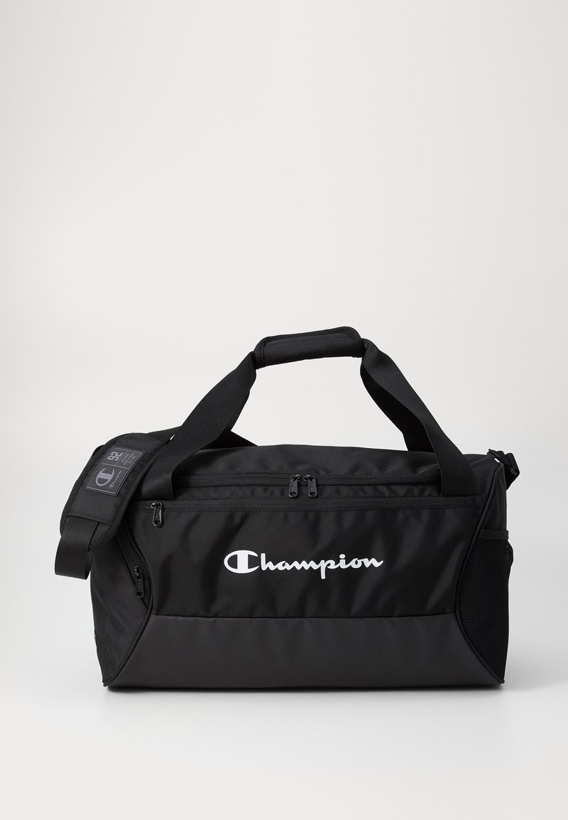 Black duffel bag with dual top handles and adjustable shoulder strap. Features Champion logo, zippered main compartment, and side mesh pocket.