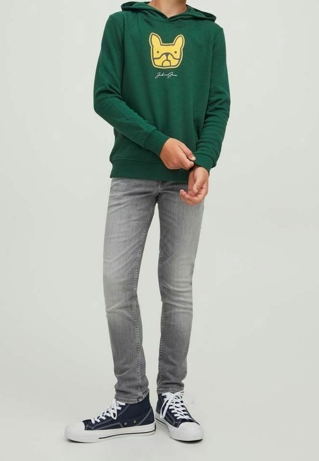 Groene hoodie met een gele hondenafbeelding, gecombineerd met slim-fit grijze spijkerbroek en marineblauwe sneakers met witte veters en rubberen zolen.