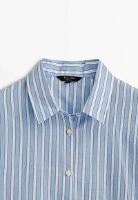Chemise bleu clair à rayures blanches verticales, dotée d'un col classique et de trois boutons visibles au niveau du col.
