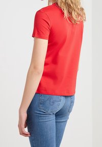 Camiseta corta roja de algodón, diseño ajustado, con un escote redondeado. Combinada con unos jeans de mezclilla azules con detalles de costura sutiles.