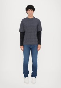 Krekli ar īsām piedurknēm, tumši zils ar rakstu, uzvilkts virs melna krekla ar garām piedurknēm, saskaņots ar ziliem džinsiem un baltiem kedām. Vienkāršs un ikdienišķs apģērbs.