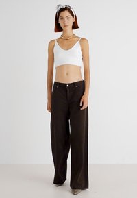 Top scurt alb, asortat cu pantaloni larghi, de culoare maro închis, cu talie înaltă și buzunare laterale. Modelul poartă un colier.