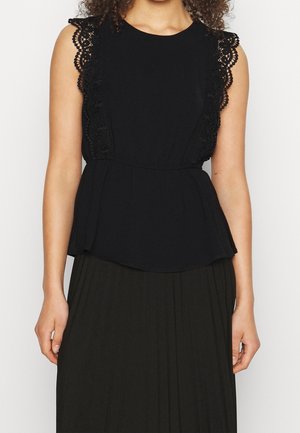 Femme portant un haut noir sans manches avec une bordure en dentelle aux épaules et une taille cintrée, associée à une jupe plissée noire.