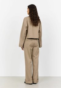 Beige Jacke mit langen Ärmeln, gekürzt und kombiniert mit weiten beigen Hosen. Glattes Material mit einem schlichten Design und ohne sichtbare Verschlüsse.