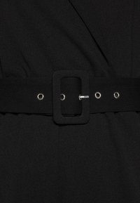 Robe en tissu noir ceinturée, dotée d'une large ceinture avec une boucle rectangulaire, des œillets métalliques et une texture lisse.