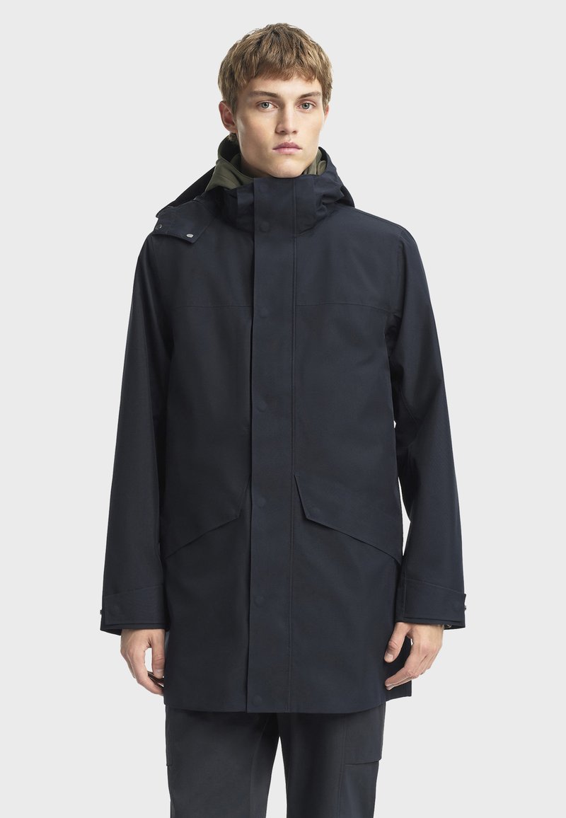 Námořnická voděodolná bunda s kapucí, předním zapínáním na cvočky a dvěma velkými kapsami, navržená v uvolněném střihu s hladkou texturou.