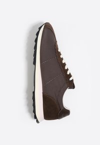 Zapatilla marrón con cordones blancos, acentos de ante en el talón y la puntera, y suela negra estriada, vista de lado sobre un fondo blanco.