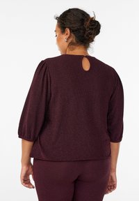 Burgundy paita, jossa on herringbone-kuvio, kolmannen osan hihat, pyöreä pääntie ja avainreikätaipeen yksityiskohta takana nappisuljennalla.