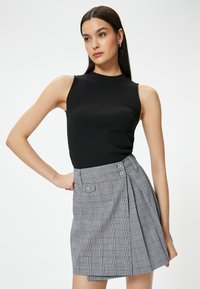 Top sin mangas negro de material acanalado combinado con una falda corta de cuadros con acentos rojos, botones y pliegues en una gama de colores gris.