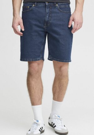 Shorts in denim blu scuro con taglio dritto, design a cinque tasche, orli cuciti e dettagli in metallo. Indossati con calze sportive bianche e scarpe.