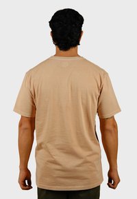 Korte mouwen beige T-shirt van zacht materiaal, met een ronde halslijn en gestikte zoom, weergegeven vanaf de achterkant tegen een effen achtergrond.