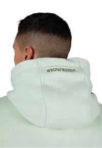 Felpa verde menta con colletto alto e logo ricamato "WRONGFRIENDS" sulla schiena. Tessuto morbido, vestibilità comoda e superficie liscia.
