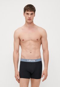 Črne boksarice iz mehkega blaga, z sivo elastiko z logotipom Levi's. Oblikovanje je oprijeto z gladko teksturo.