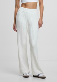 Gestreifte, hochtaillierte weite Hosen in Off-White. Weicher Stoff mit vertikalem Muster. Kombiniert mit grauen und weißen Sneakers.