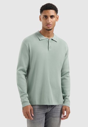 Lichtgroen poloshirt met lange mouwen van zachte stof, voorzien van een puntige kraag en een knoopsluiting met drie knopen, gecombineerd met grijze jeans.