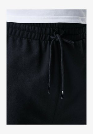 Musta collegehousut, joissa on nyöri ja metalliset päätykappaleet, sileä pinta ja joustava vyötärönauha mukavuutta varten.