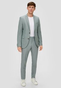 Lichtgrijs op maat gemaakt pak met een enkelgebreide blazer en bijpassende broek, gecombineerd met een wit t-shirt en witte sneakers. Glad oppervlak.