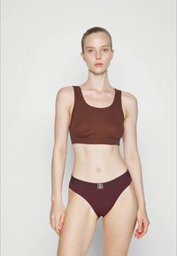 Top cropped castanho com nervuras e alças largas, combinado com um fundo de bikini de cintura alta a condizer, apresentando um logótipo. Textura suave, design ajustado.