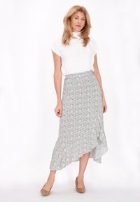 Witte top met korte mouwen, gecombineerd met een zwart-wit gestreepte, asymmetrische rok met een gerimpelde zoom en beige hakken.