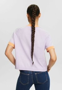 Fioletowy sweter z krótkim rękawem i pomarańczowymi ściągaczami, luźny krój. Połączony z ciemnoniebieskimi dżinsami, modelka pokazana od tyłu z długim warkoczem.