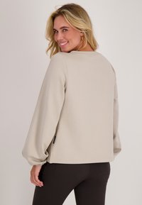 Beige sweatshirt met lange, geplooide mouwen, ronde halslijn en elastische manchet. Gelaagde stof met zijsplitten aan de zoom.