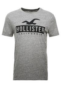 Camiseta de manga corta gris hecha de una mezcla de algodón con un logo negro "HOLLISTER CALIFORNIA" en el pecho en una fuente negrita.