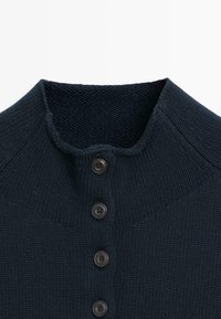 Dunkelblauer Strickcardigan mit Rundhalsausschnitt und vier schwarzen Knöpfen vorne, der die detaillierte Struktur des Stoffs zeigt.