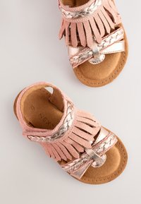 Sandali in suede rosa con dettagli intrecciati metallici e frange. Cinturini morbidi e testurizzati e soletta imbottita marrone.