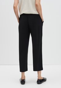 Zwarte cropped broek met een relaxte pasvorm, voorzien van zijzakken, een elastische tailleband en een gladde stofafwerking.