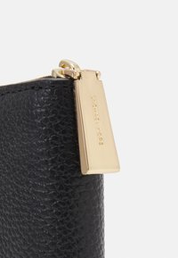 Black leather wallet with textured surface and gold hardware zipper pull, featuring engraved brand name detail.