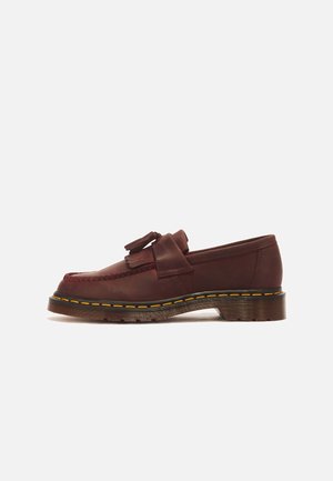 Brauner Leder-Tassel-Loafer mit gelber Nahtdetail, dicker gerillter Sohle und niedrigem Absatz, seitlich vor weißem Hintergrund gezeigt.
