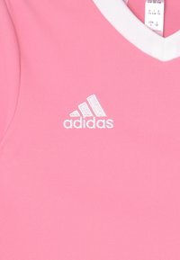 Rosa idrottstopp med vit V-ringning. Har broderad vit Adidas-logga. Slät, elastisk tyg med inga synliga mönster.