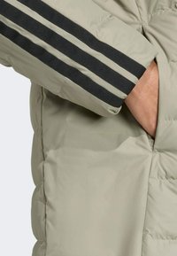 Doudoune beige clair avec des accents rayés noirs sur les manches, dotée d'une texture lisse et d'une poche latérale pour plus de praticité.