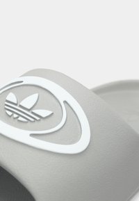 Hall halliga liblikatingimust sussid tekstureeritud kummist pinnaga. Rihmal on valge logo, millel on kolm triipu ja lehekujuline disain. Lihtne, kaasaegse kujuga.