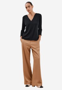 Schwarze V-Ausschnitt-Bluse mit 3/4-Ärmeln, kombiniert mit beigefarbenen, weiten Hosen und zweifarbigen Ballerinas. Glatter Stoff, lockere Passform.